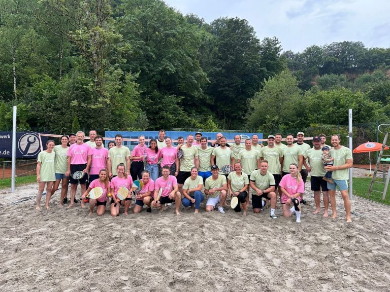 Beach&Beat 2024 Gruppenfoto von Volleyballspielern in bunten Shirts auf Sandplatz.